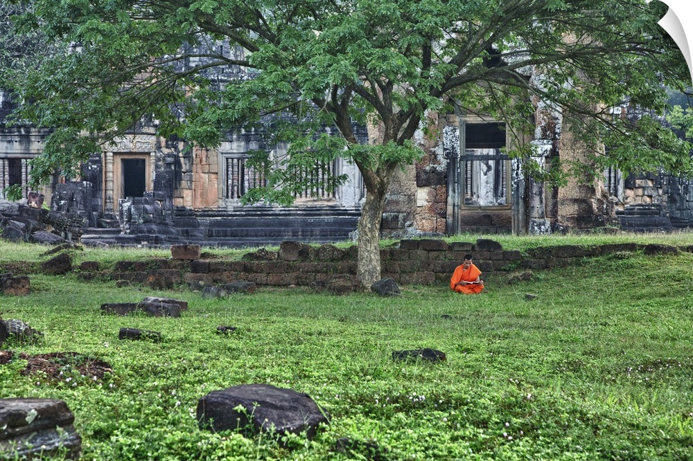 Monk reading in grass in front of religious temples in Angkor Wat, Cambodia