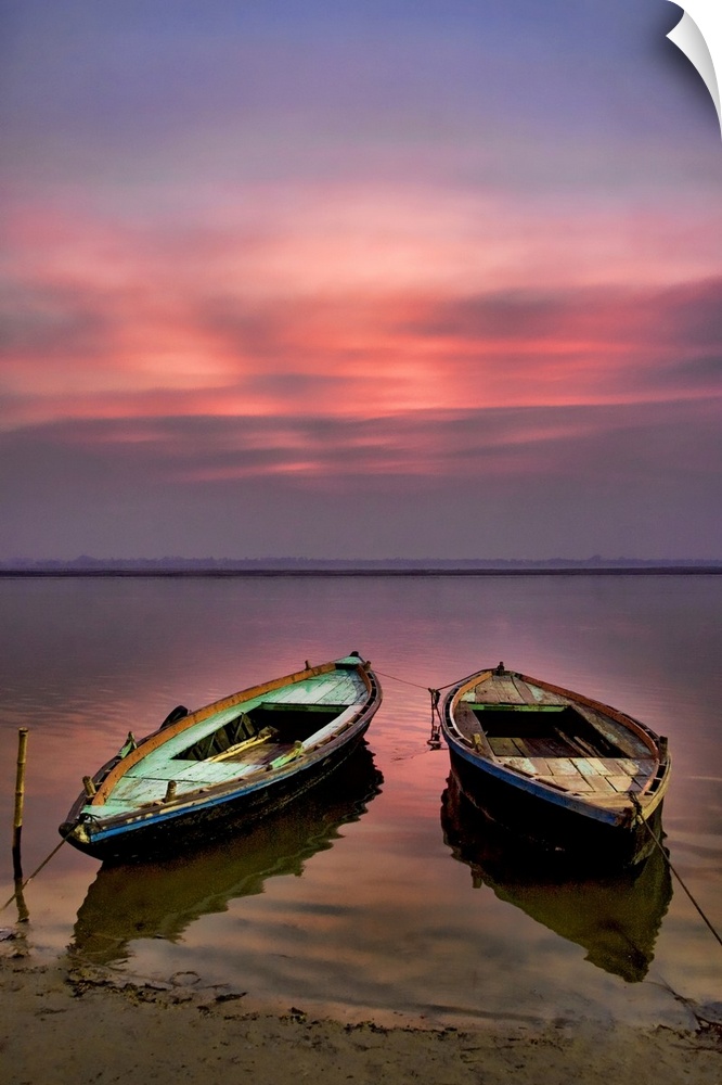 Picture of two empty wooden boats tied to the sandy shore in the early morning sunrise.