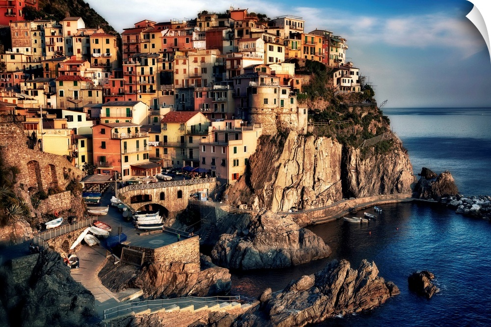 A small town sits in and on a cliff right near the water. The sun has begin to set shining brightly onto the houses.