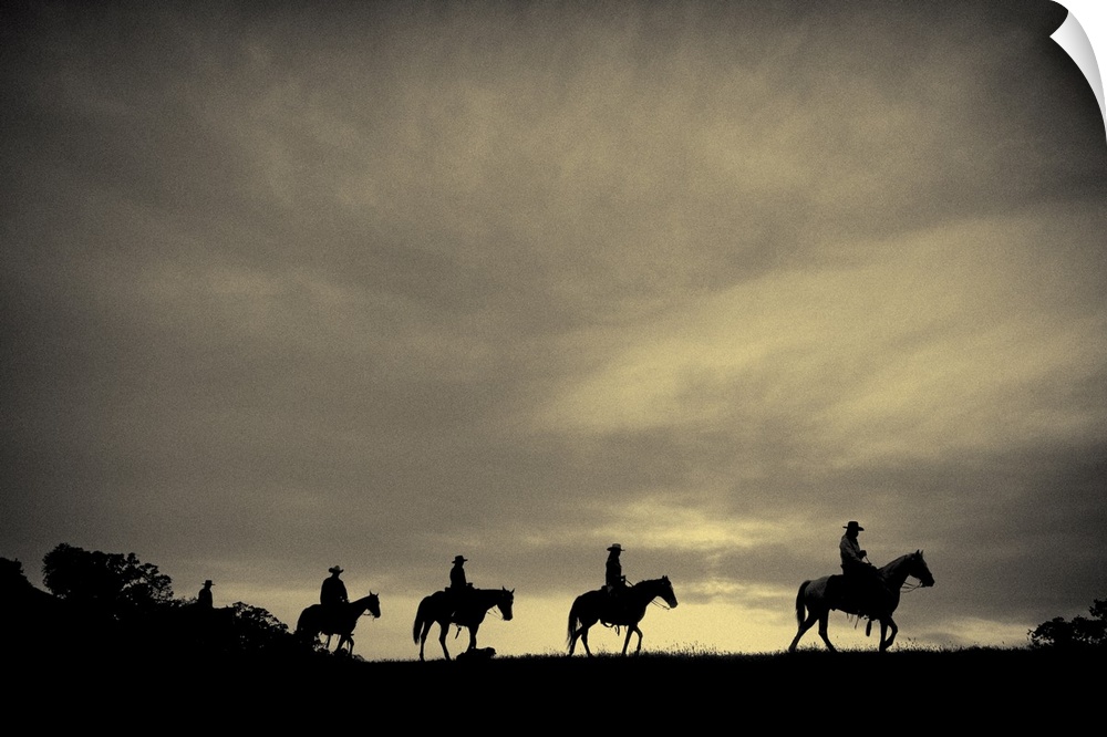 Sepia-toned photo of four cowboys on horseback silhouetted against an overcast sky.