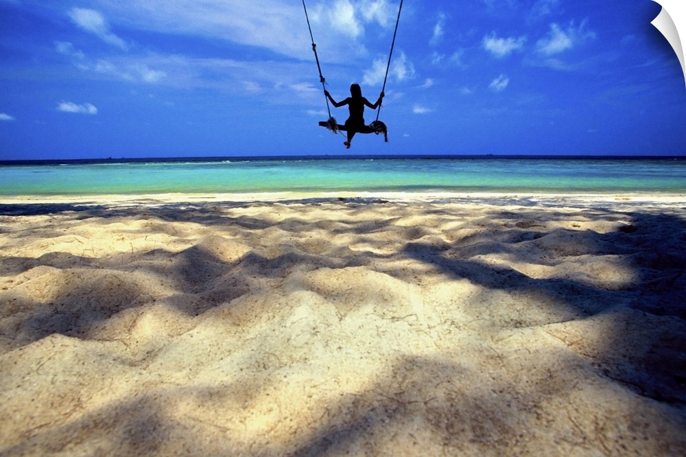 landscape, large photograph of the silhouette of a woman on a swing over the sandy beach, looking out toward crystal blue ...