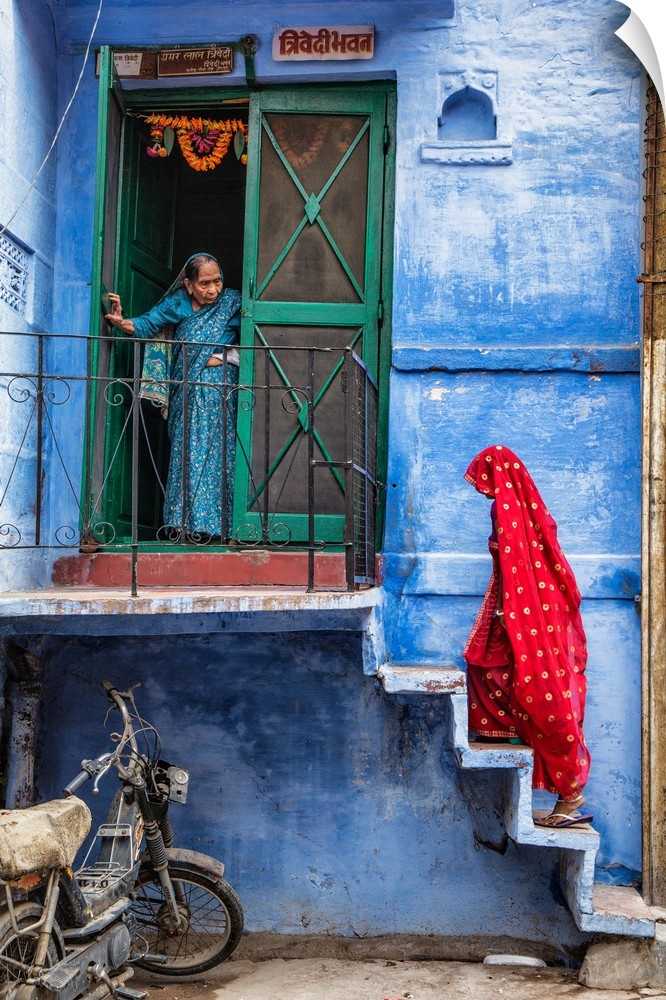 Woman with red Sari walking up steps in the blue city of Jodphur, India.