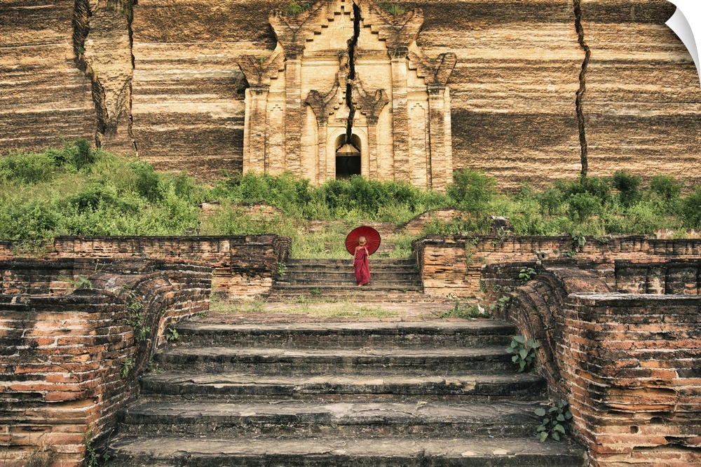 Young Burmese monk boy walking with parasol by his monastery.