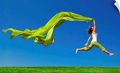 Young woman jumping on a green meadow with a green scarf
