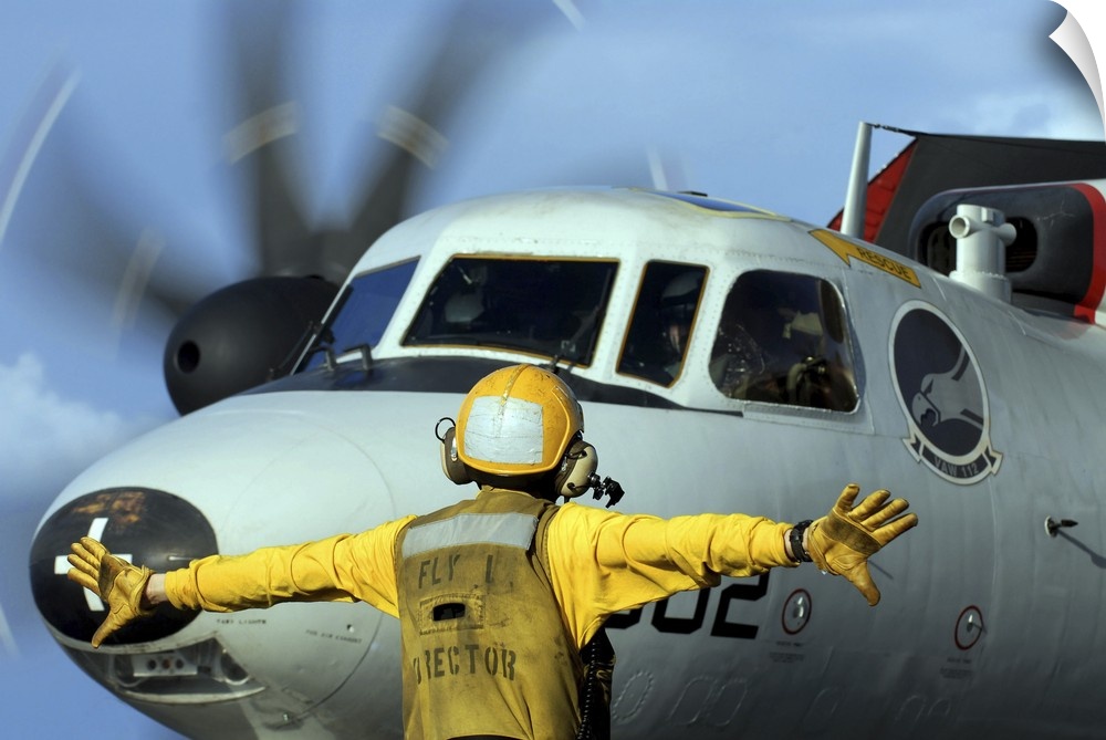 A flight deck director signals the pilot of an E-2C Hawkeye to spread his wings.