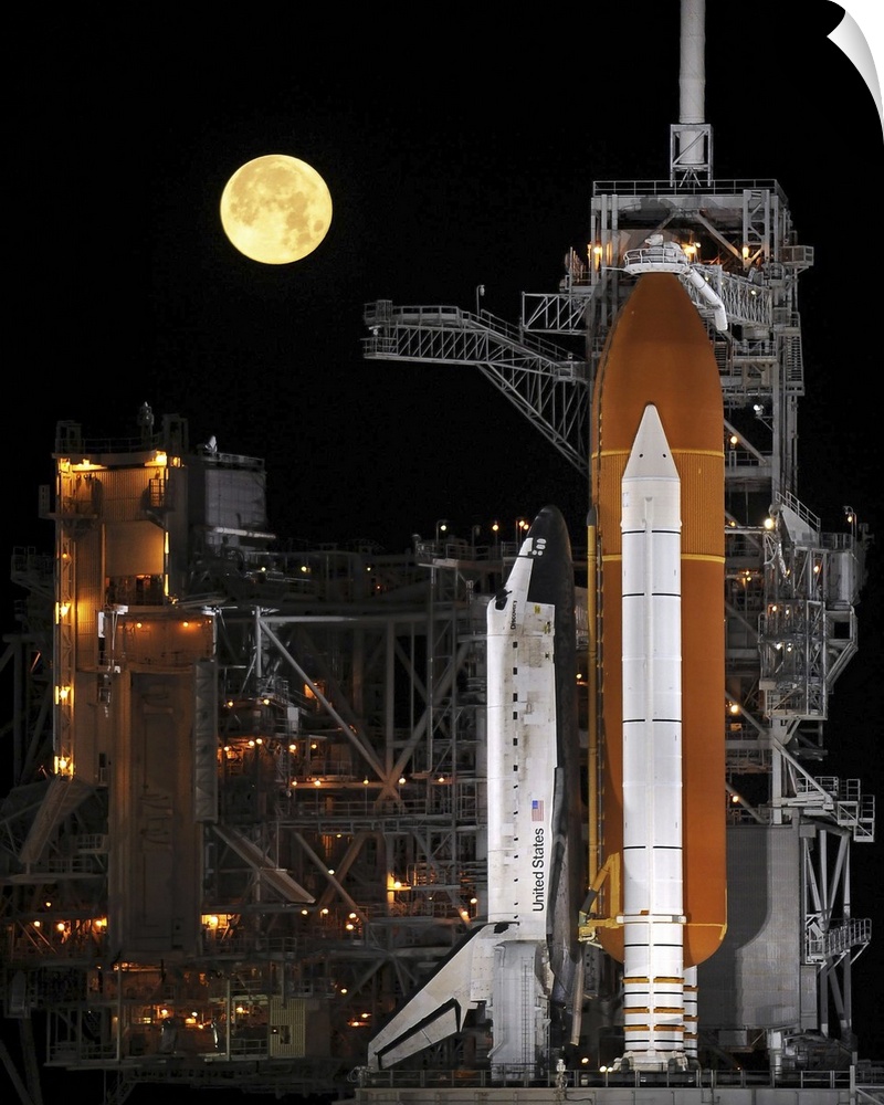 A nearly full Moon sets as Space Shuttle Discovery sits atop the launch pad