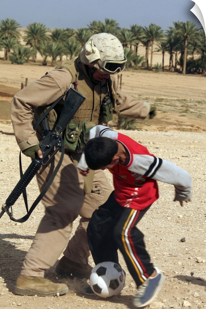 A soldier plays soccer with an Iraqi boy.