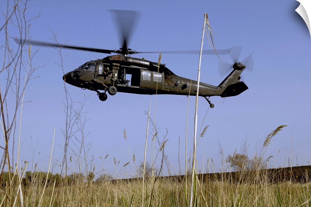 Photograph taken of a helicopter as it lifts off in a tall grass field.