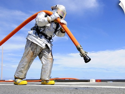 Firefighter Carries A Charged Hose Across The Flight Deck Of USS Denver