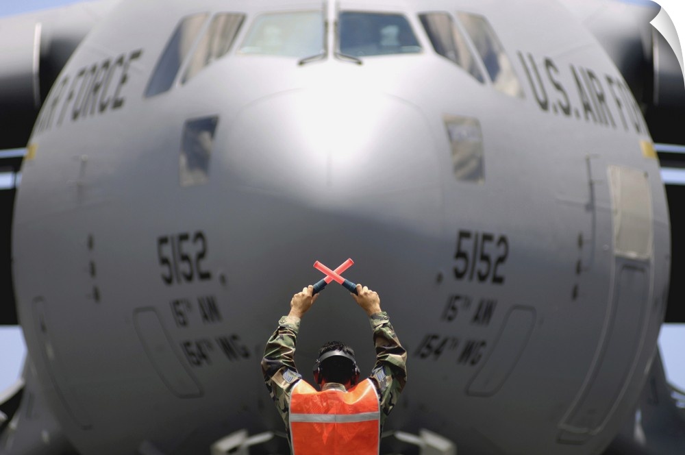 Ground crewmember marshals a C-17 Globemaster III to its parking spot.