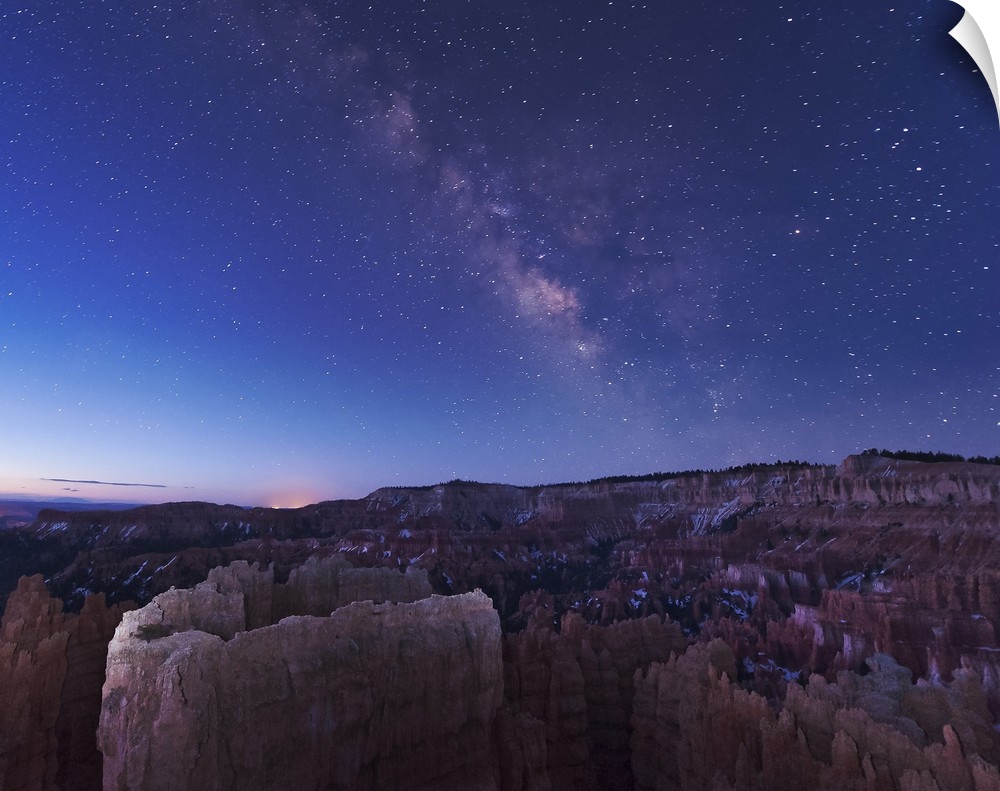The rising sun begins fading away the nightime Milky Way over the needle rock formations of Bryce Canyon, Utah.