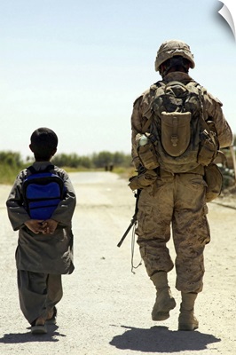 Rear view of US Marine walking through Nawa bazaar with an Afghan boy in Afghanistan