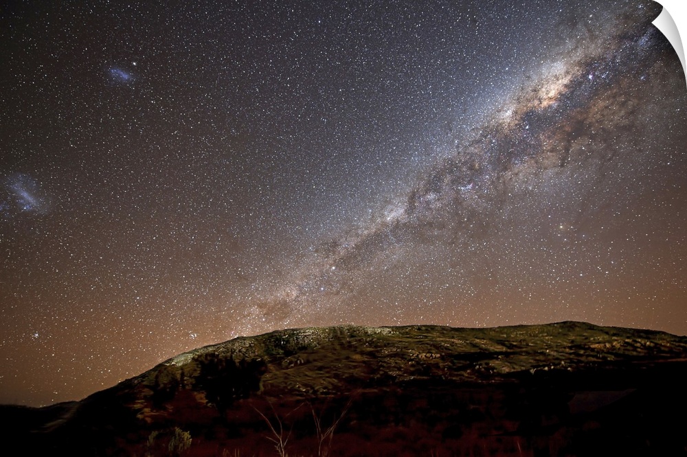 The Milky Way and its satellite galaxies the Magellanic Clouds rising above the hills of Azul, Argentina.