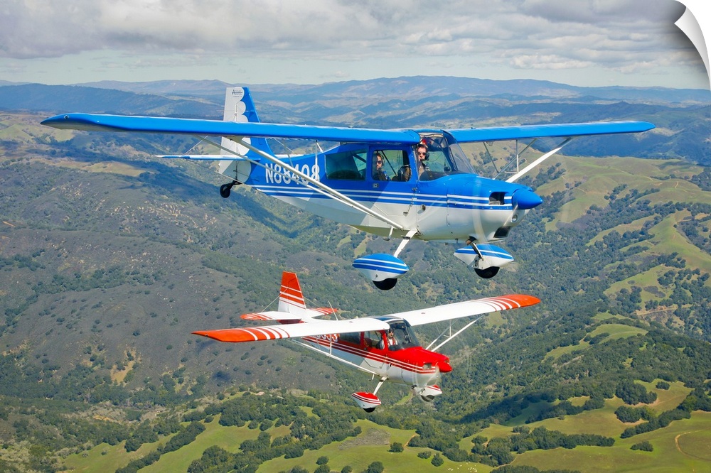 Two small airplanes are photographed while in flight over vast open land.