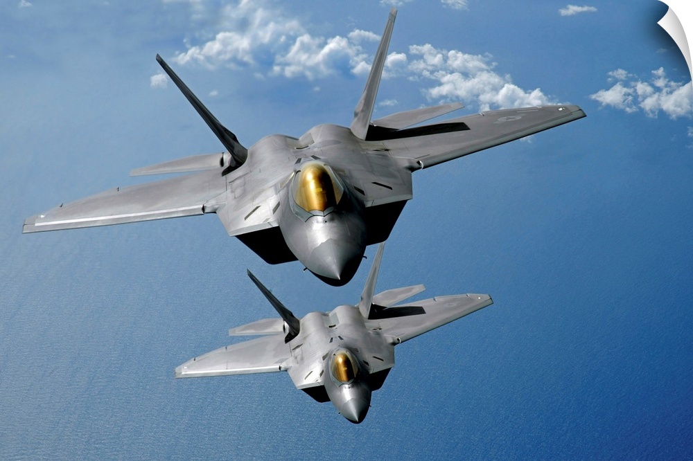 Large, landscape photograph of two F22 Raptors flying high in the sky above the blue waters of the Pacific Ocean.