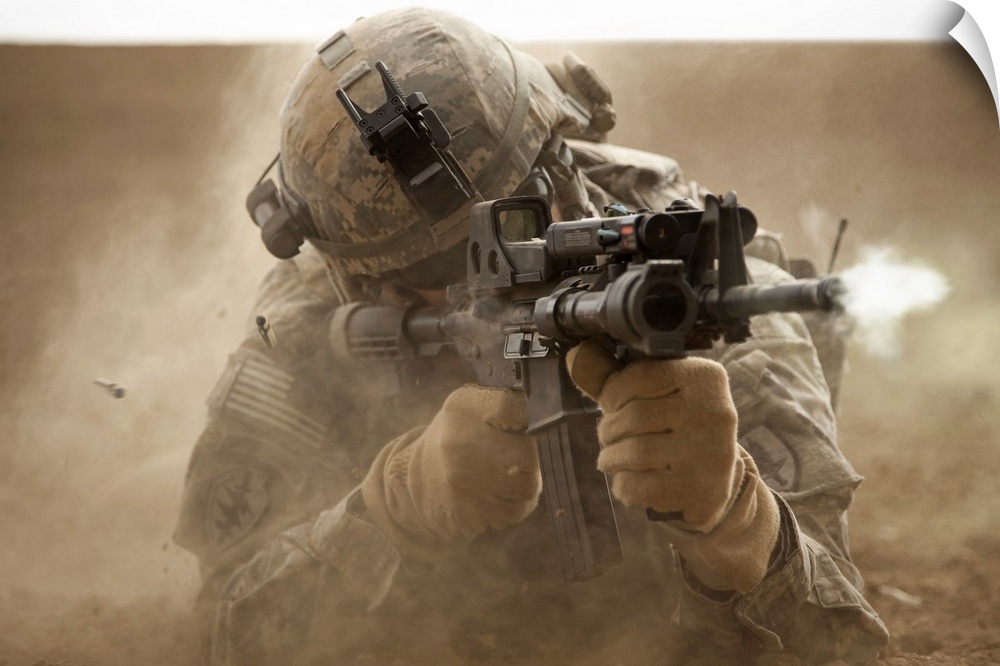 United States solider laying down in the desert sand and shooting a military rifle.
