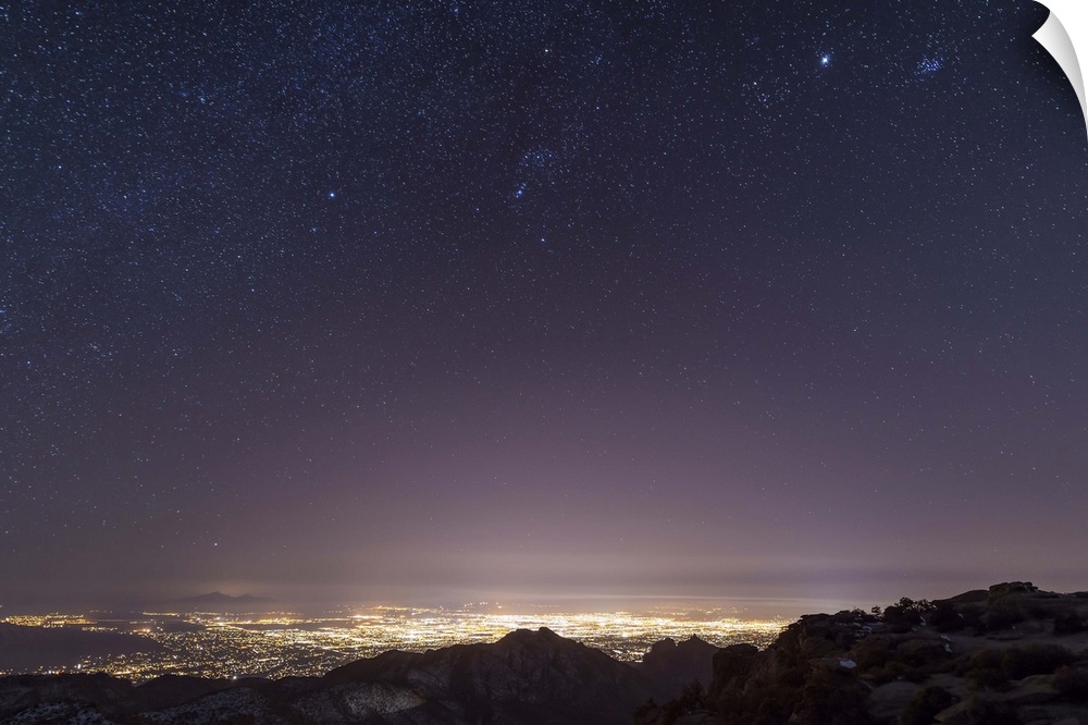 A view from midway up Mount Lemmon, looking down into Tucson, Arizona. Orion, Jupiter, and the Pleiades float above the ci...