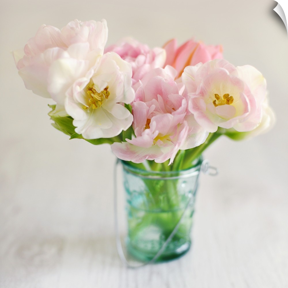 Square photograph of arranged pink and white flowers in a blue toned mason jar on a wooden table.