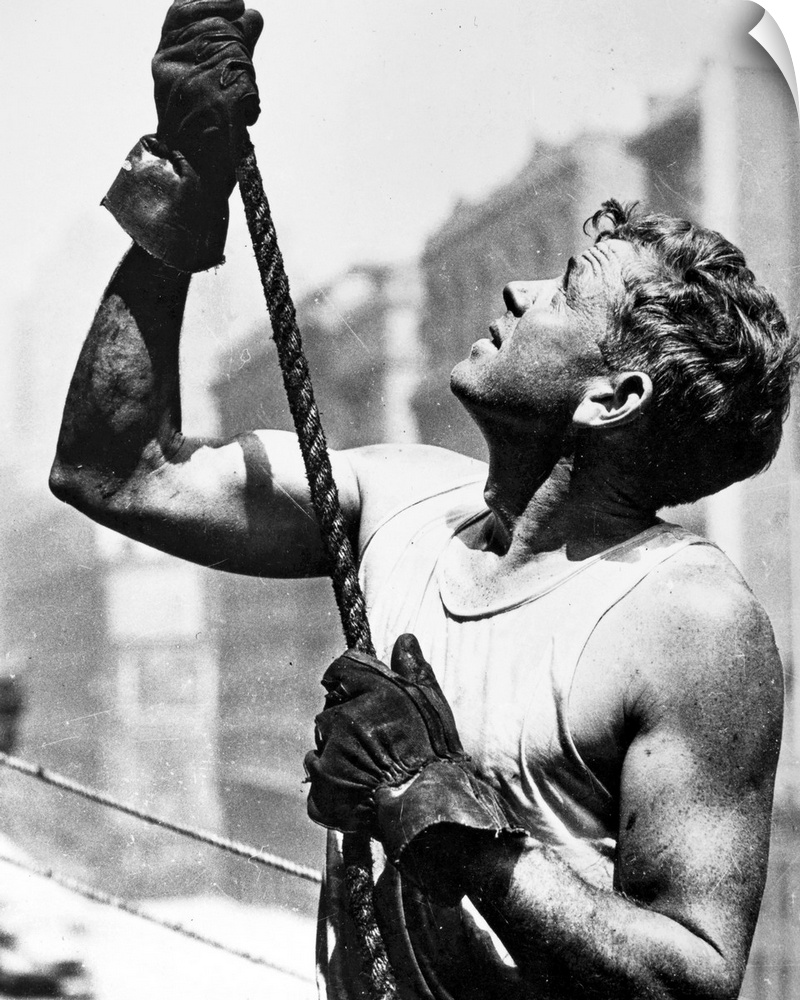 A construction worker gripping a rope at work on the Empire State Building in New York City. Photograph by Lewis W. Hine, ...