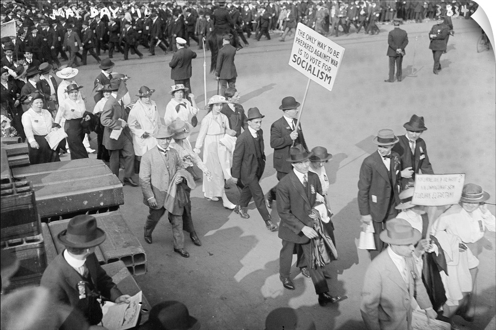 Women and men marching at the May Day Parade as one man holds a sign promoting Socialism in New York City. Photograph, 1916.
