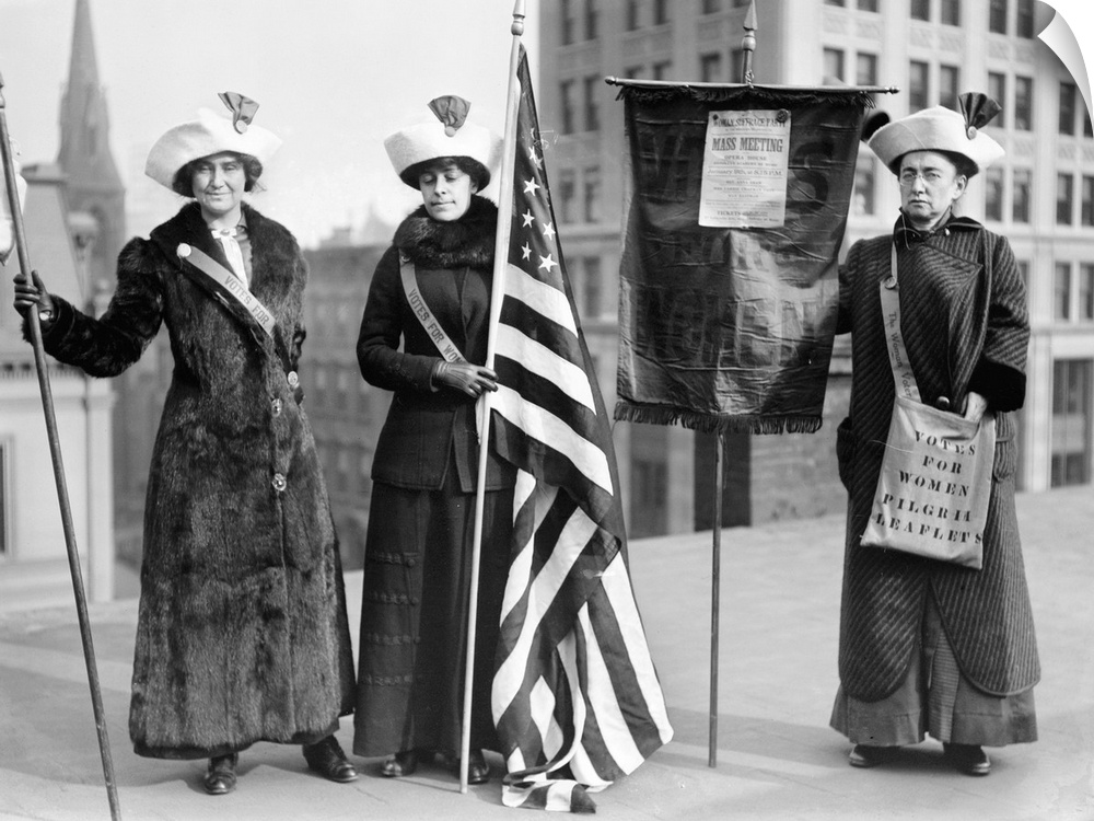 Three women photographed on a Brooklyn rooftop before a demonstration for women's right to vote. One woman holds a poster ...