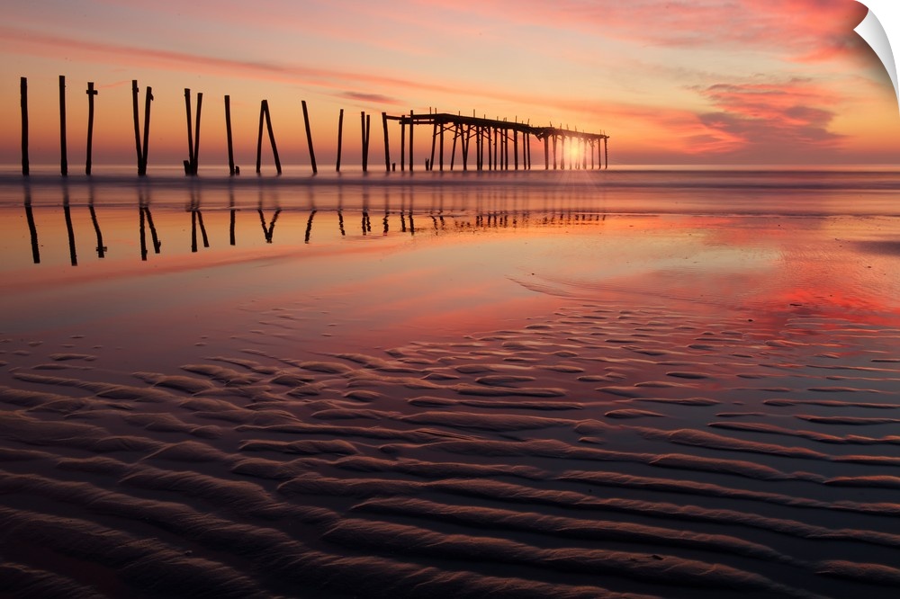 Old wooden pier seen from the beach during a dramatic sunset.