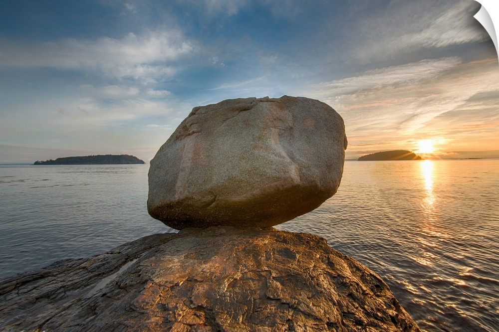 A large rock on the beach in Acadia National Park in Maine, with the sun rising in the distance.
