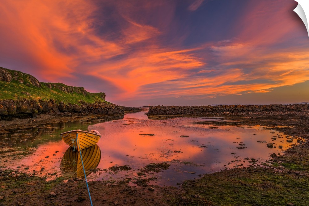 A canoe moored at low tide under vivid sunset clouds in Iceland.
