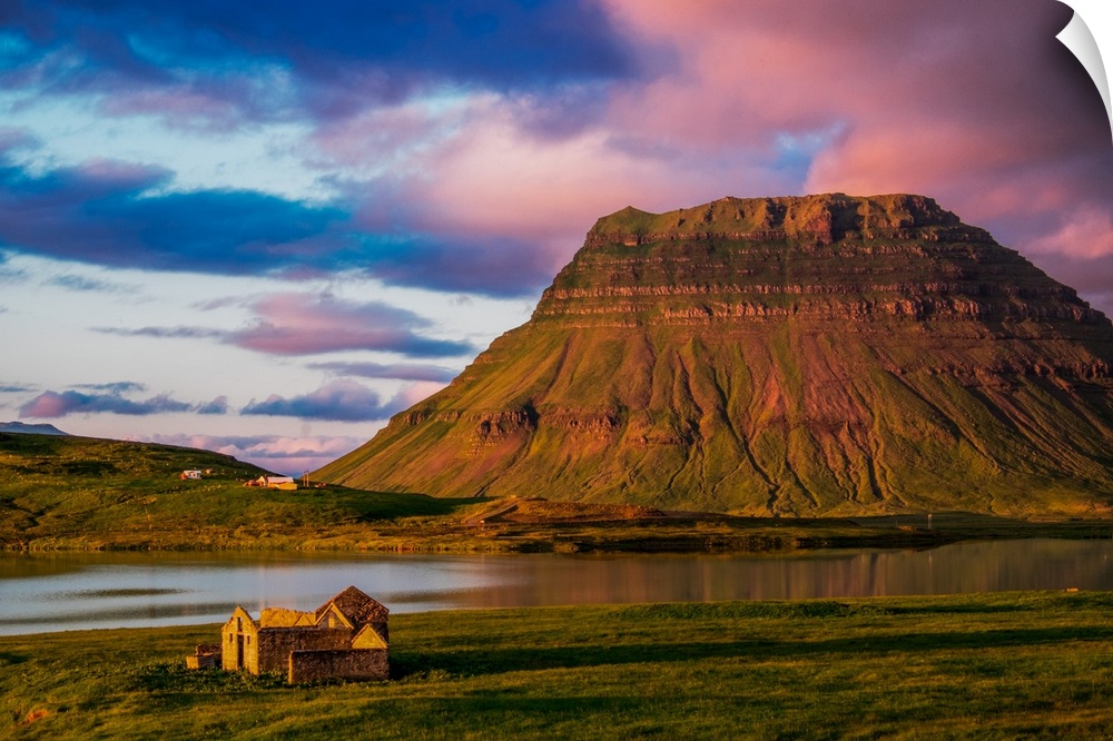 A small house near a mountain with pink clouds at sunset in Iceland.