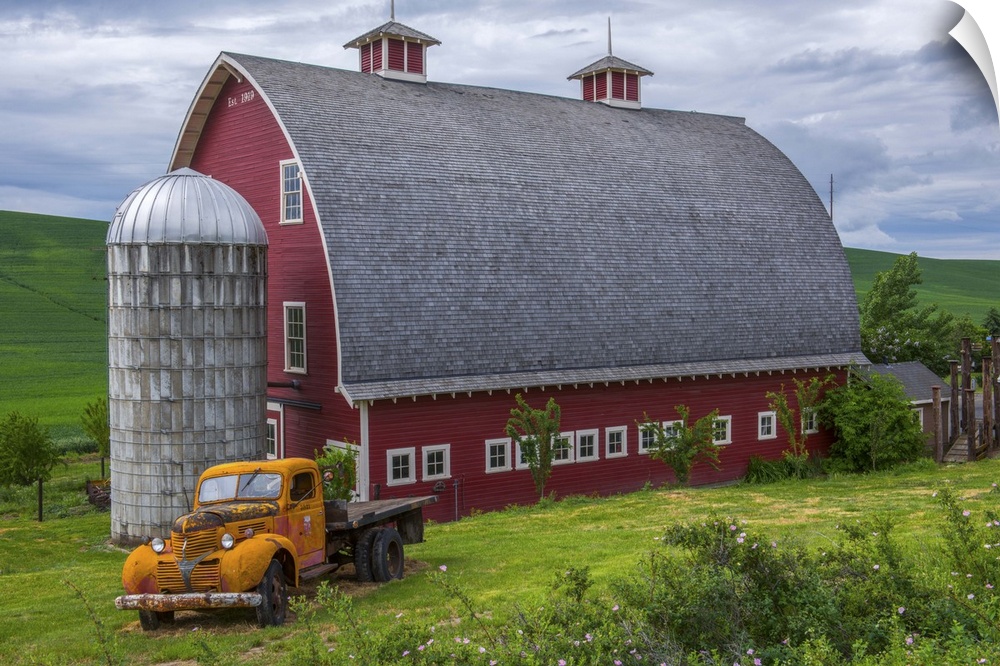 A large red barn and an orange truck against the green landscape of Palouse, Washington.