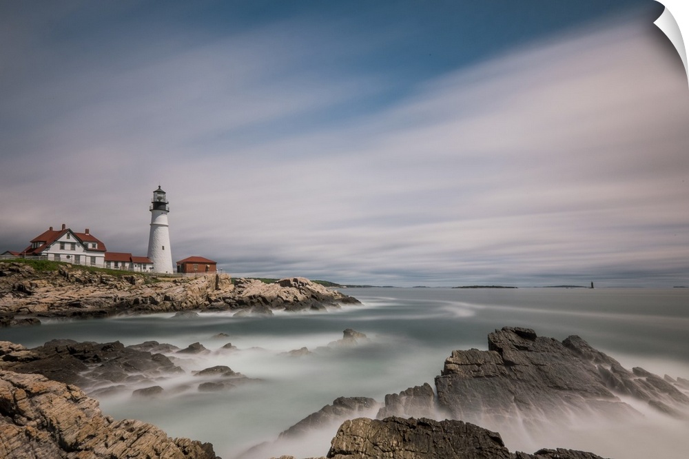 Lighthouse on the rocky coast of Maine with sweeping clouds above.