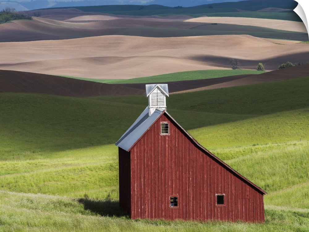 Lone red barn in a green field in the hills of the Idaho countryside.