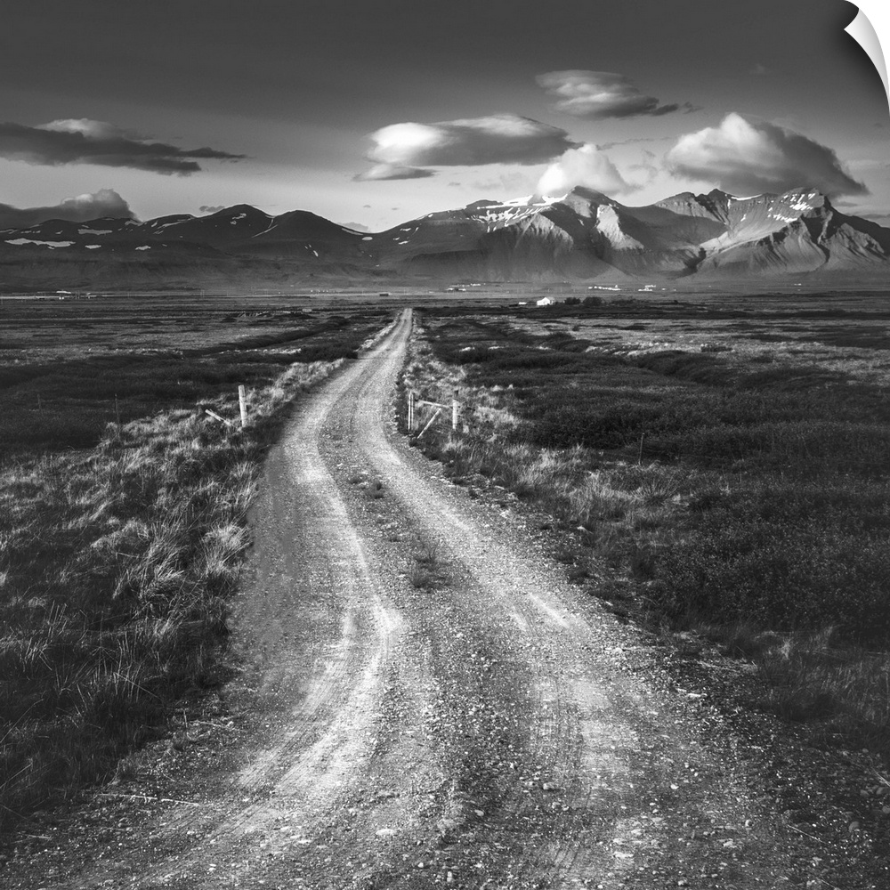 Black and white photo of a path leading to tall mountains on the horizon.