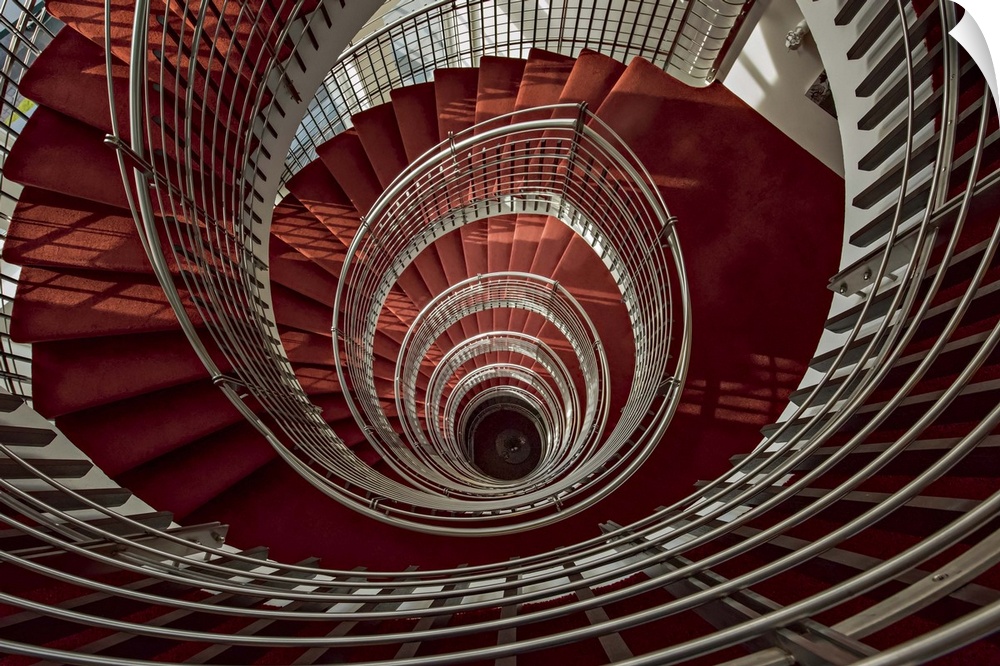 View through the center of a spiral staircase with red steps and white railings.