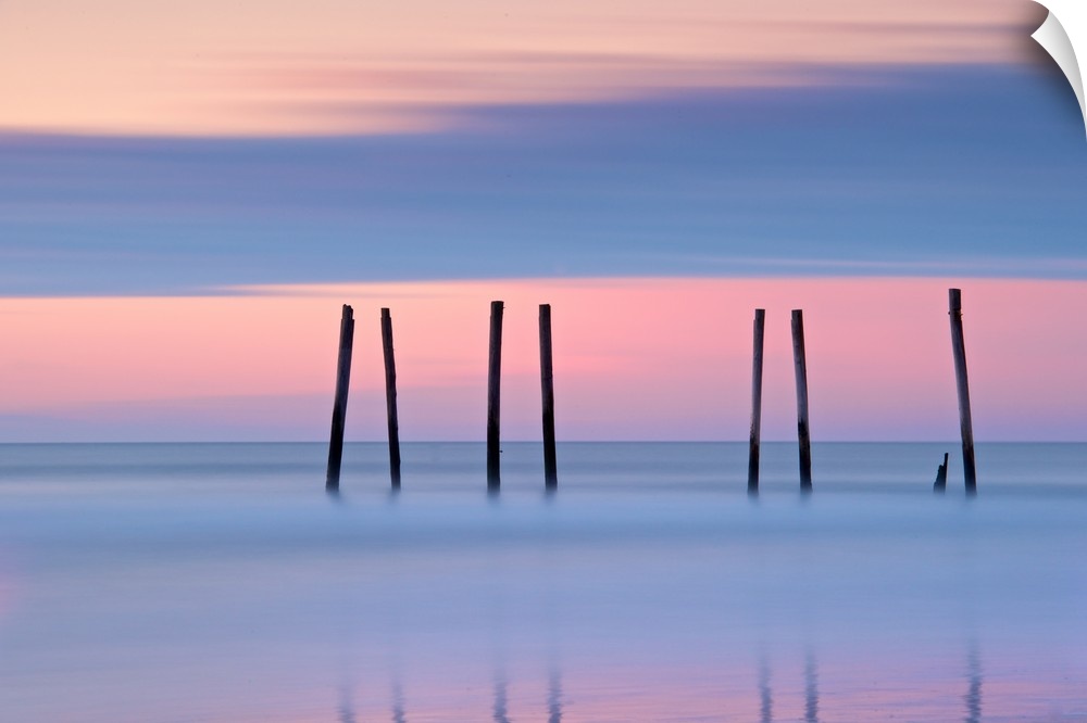 Silhouettes of seven pilings in the ocean at sunset in New Jersey.