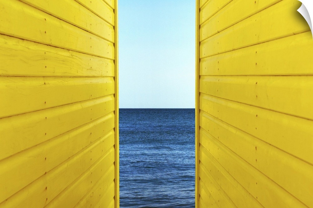 Symetrical perspective of 2 Yellow Beach Huts with blue sky and sea inbetween them.