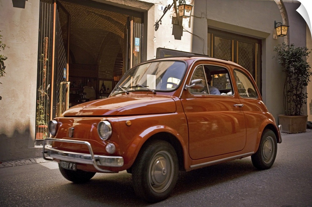 A small red car drives through the narrow streets in the downtown area of an Italian city.