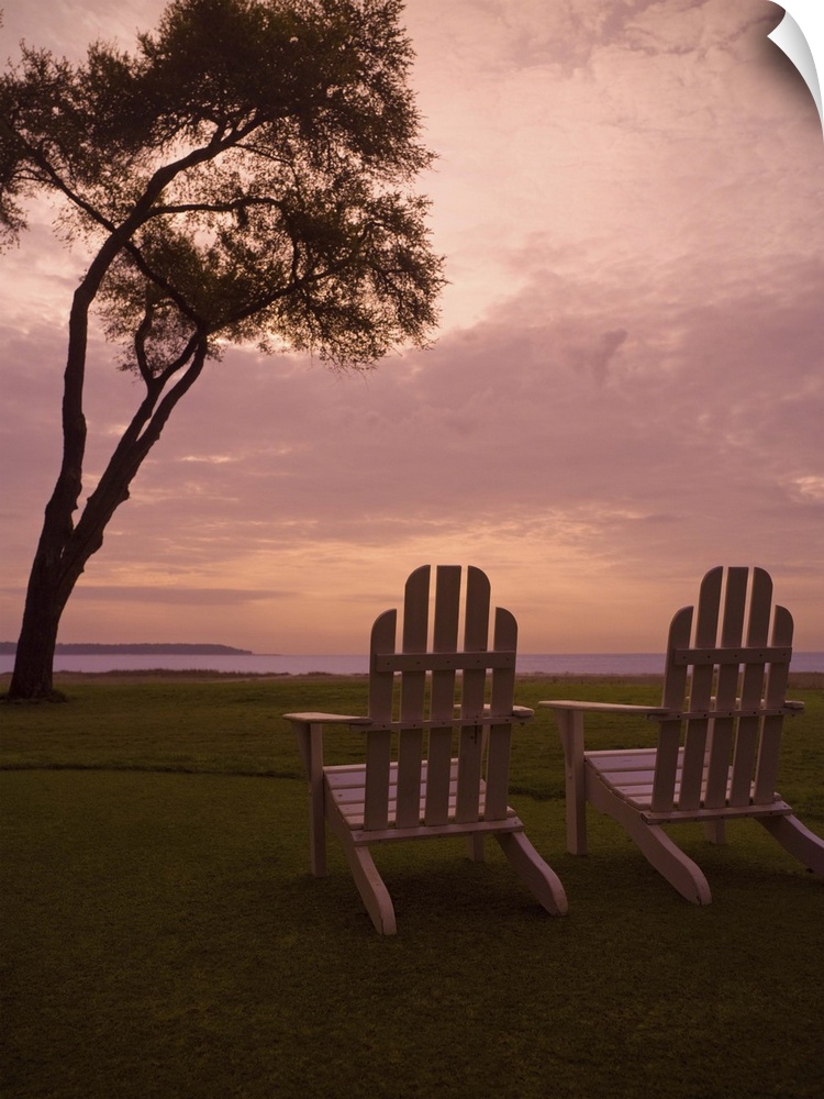 Adirondack chairs sit on a grassy field at sunset.
