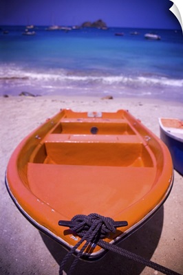 An colorful orange row boat on a Caribbean beach in front of the turqoise Caribbean Sea