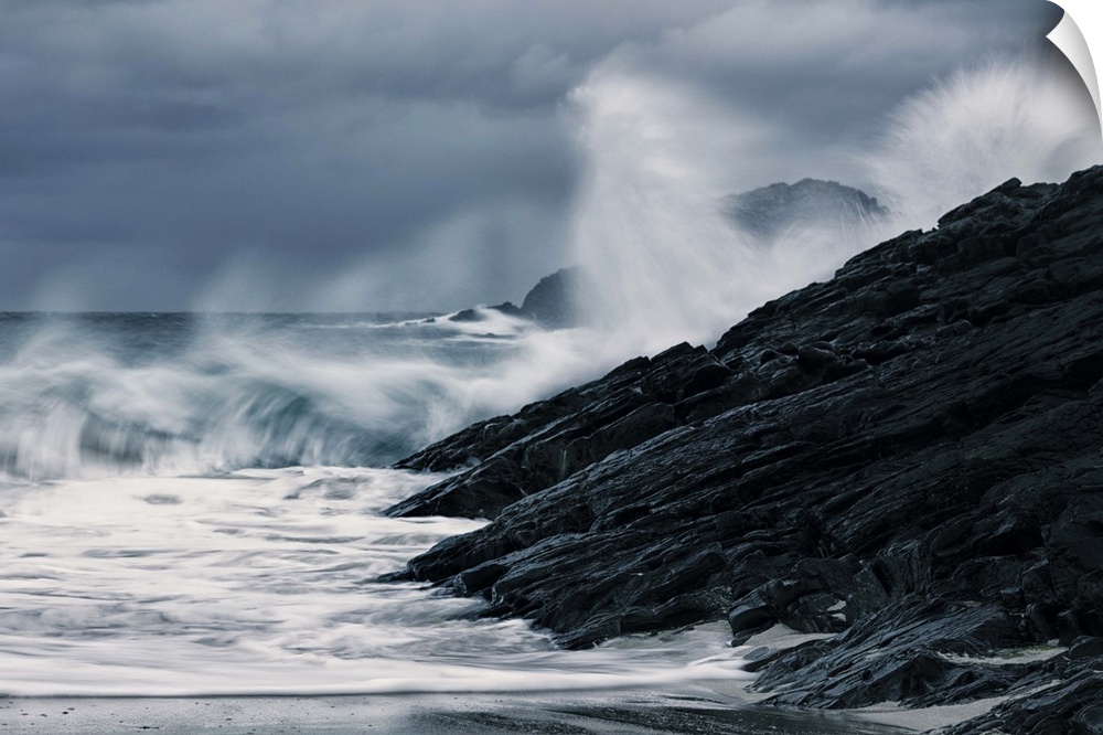 Crashing waves on a stormy Scottish beach with dark rocks under grey sky