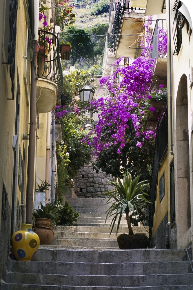 Decorations including vases and flowers line the steps of a residential alleyway in Taoramina, Italy