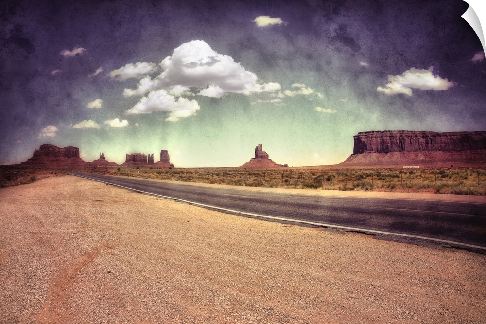 Large monolithic rocks in the background looking through Monument Valley in the United States, with desertic road and clou...