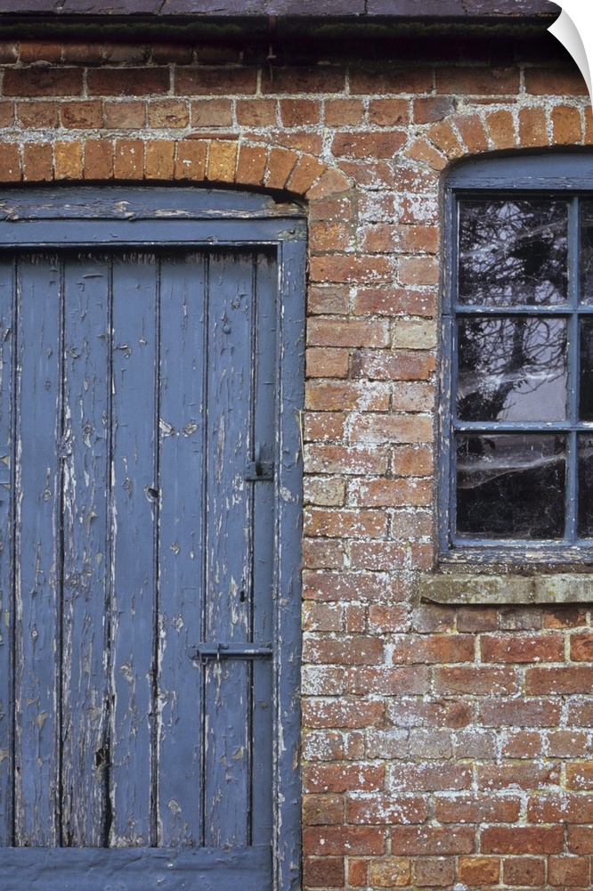 Detail of old orange brick stable block or barn with flaking blue painted wooden door and windows and slate roof