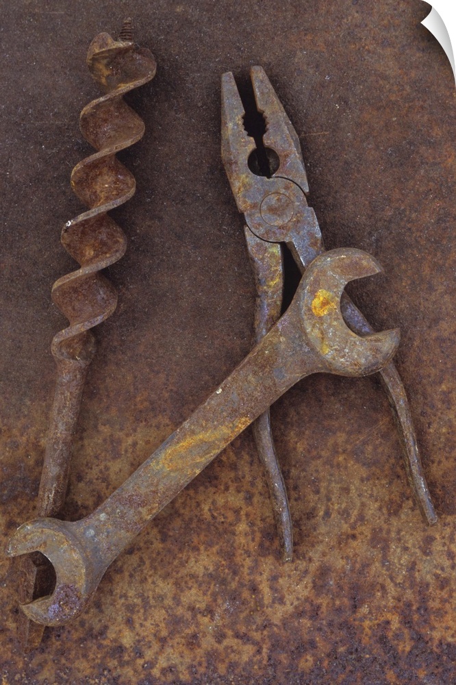 Rusty old double-headed spanner lying next to large drill bit and rusty pliers on rusty metal sheet