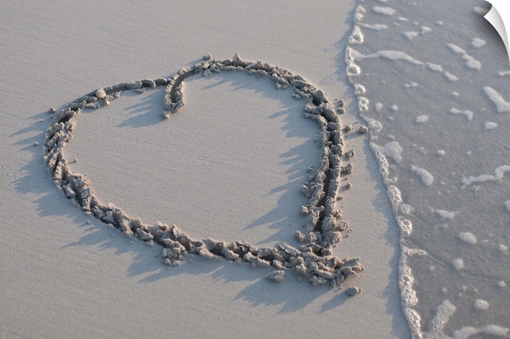 A heart drawn in the sand with the tide coming in to one side