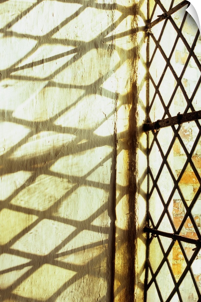Detail of stone-framed window with diamond-leaded panes of clear or pale yellow glass throwing shadows onto niche wall