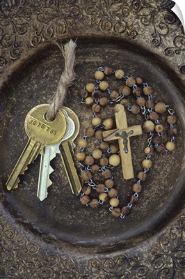 Three brass doorkeys tied with string lying next to rosary with crucifix in old bowl