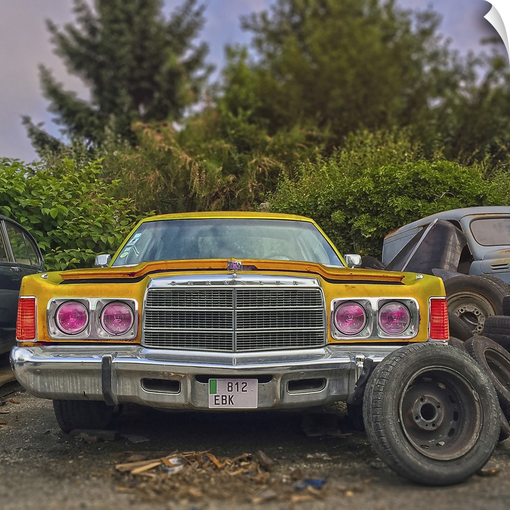 Old yellow classic Chrysler car in salvage area in USA with spare wheels.