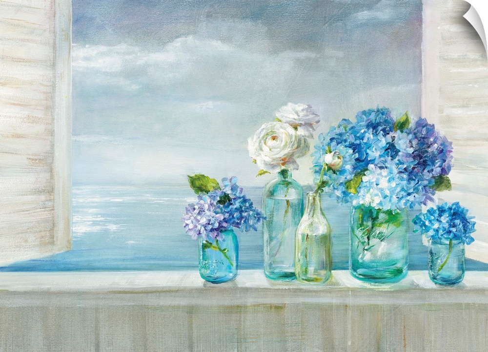 A collection of flowers in blue glass vases on a windowsill overlooking the ocean.