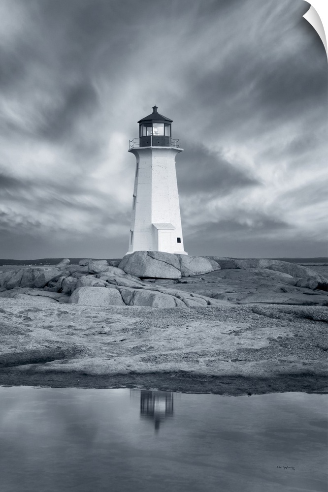 A vertical black and white photograph of a white lighthouse reflecting in the water with a dramatic cloudy sky.